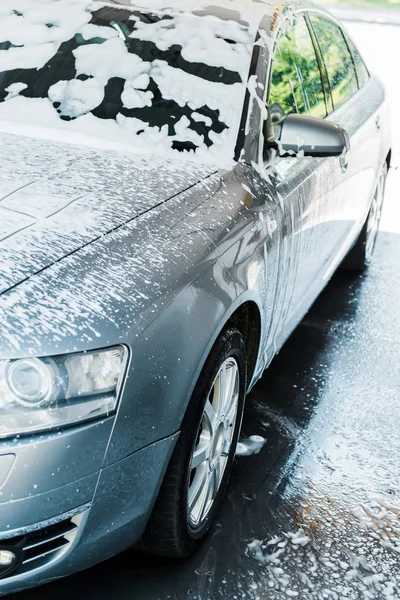 Selective focus of grey car with white foam in car wash — Stock Photo