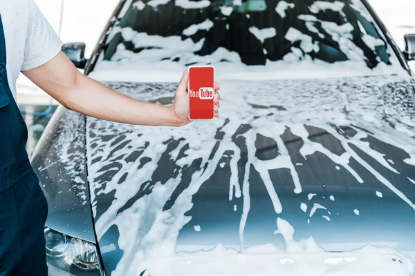 KYIV, UKRAINE - JUNE 20, 2019: cropped view of man holding smartphone with youtube app on screen near car with foam — Stock Photo