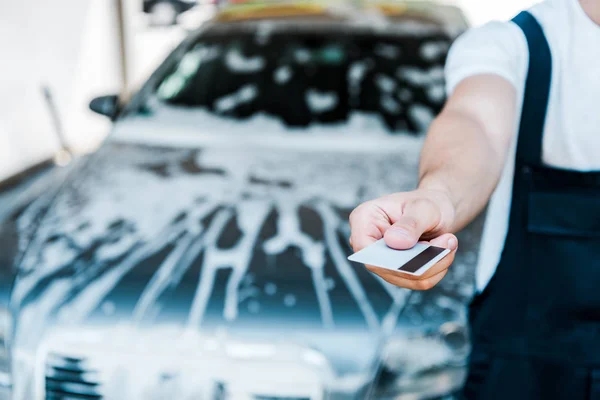 Cropped view of man holding credit card near car with foam — Stock Photo