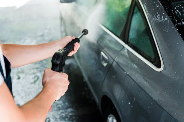 Vista ritagliata di pulitore auto tenuta rondella di pressione mentre in piedi vicino all'auto — Foto stock