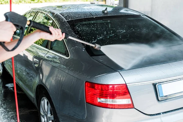 Selective focus of car cleaner holding pressure washer with water while standing near car — Stock Photo
