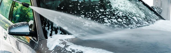 Panoramic shot of pressure washer with water on grey modern car with foam — Stock Photo