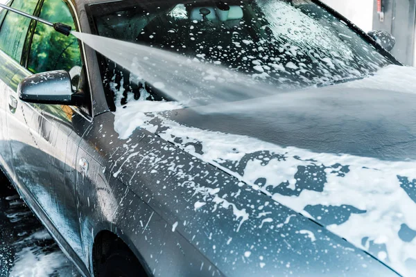 Pressure washer with water on grey modern car with foam — Stock Photo