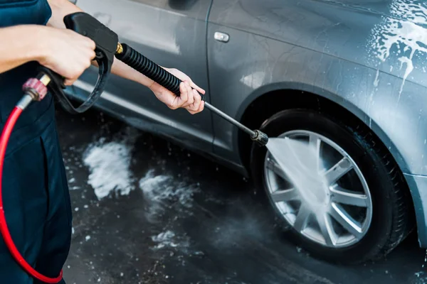 Selektiver Fokus des Mannes, der Hochdruckreiniger mit Wasser hält, während er in der Nähe des Autos steht — Stockfoto