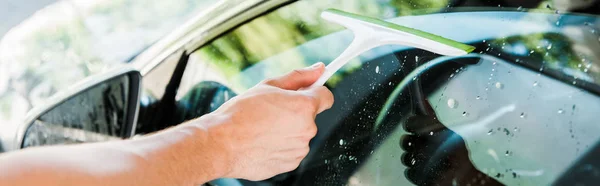 Plano panorámico del hombre sosteniendo la escobilla mientras limpia la ventana del coche - foto de stock