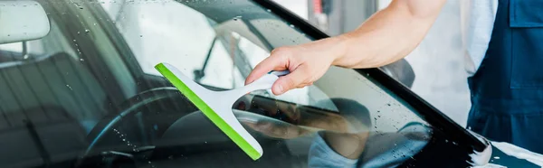 Panoramic shot of car washer holding squeegee while cleaning car window — Stock Photo