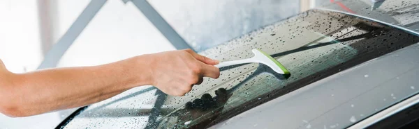 Panoramic shot of man holding squeegee and washing wet car window — Stock Photo