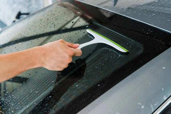 Cropped view of man holding squeegee and washing wet car window — Stock Photo