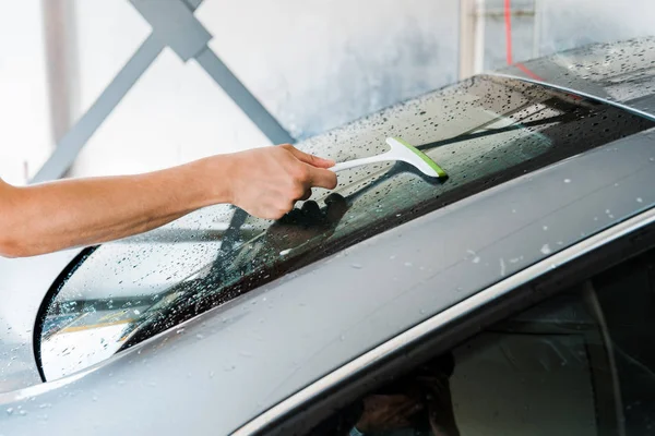 Vista recortada del limpiador de automóviles que sostiene la escobilla y limpia la ventana húmeda del coche - foto de stock