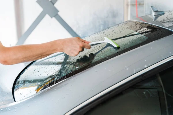 Abgeschnittene Ansicht der Autowäsche, die Rakel hält und nasse Autoscheibe reinigt — Stockfoto