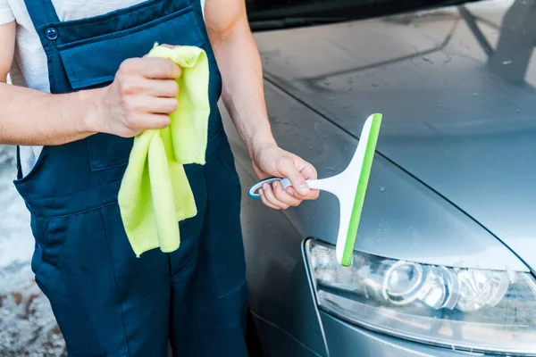 Cropped view of car cleaner holding rag and squeegee near wet car — Stock Photo