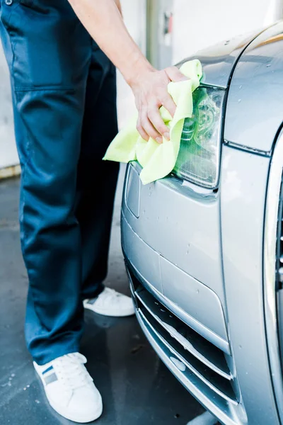 Cropped view of car washer holding green rag while cleaning car headlight — Stock Photo