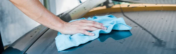 Panoramic shot of car cleaner cleaning wet car with blue rag — Stock Photo