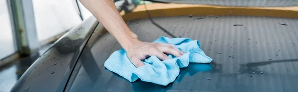 Panoramic shot of man cleaning wet car with blue rag — Stock Photo