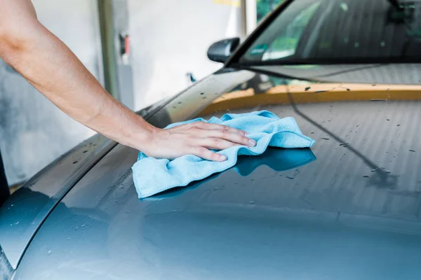 Recortado vista de hombre limpieza mojado coche con trapo azul - foto de stock