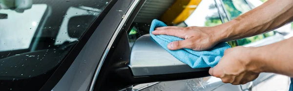 Panoramic shot of man cleaning wet car mirror with blue rag — Stock Photo