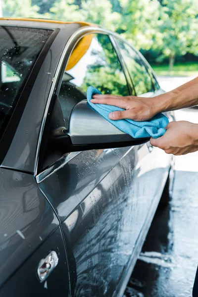 Cropped view of man cleaning grey car mirror with blue rag — Stock Photo