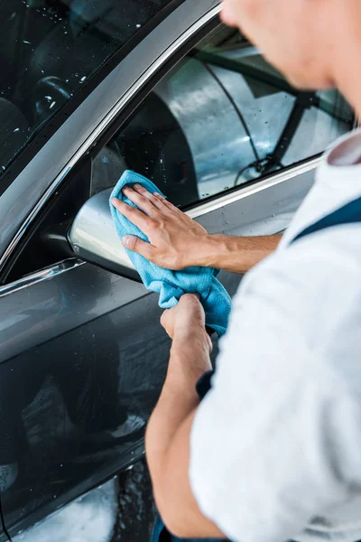 Cropped view of car washer cleaning wet car mirror with blue rag — Stock Photo