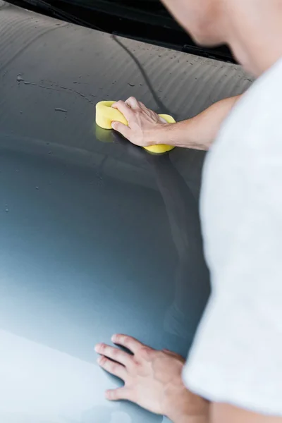 Foco seletivo do homem segurando esponja amarela durante a limpeza do carro — Fotografia de Stock