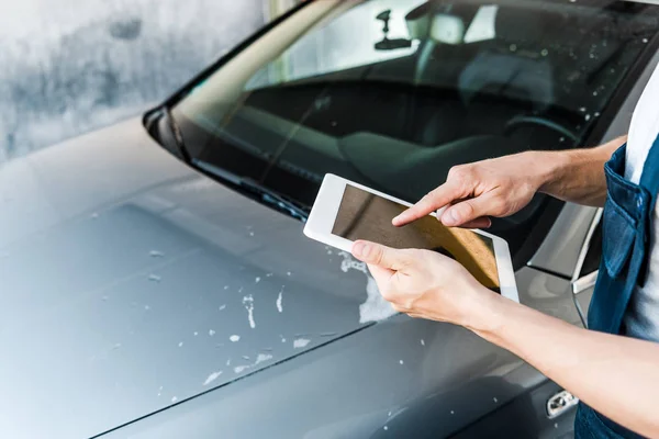 Enfoque selectivo del limpiador de coches apuntando con el dedo a la tableta digital con pantalla en blanco - foto de stock