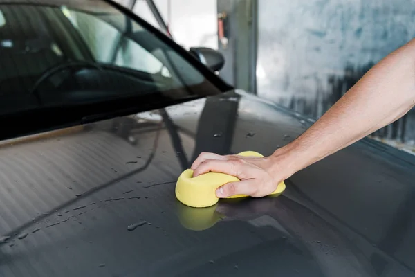Обрезанный вид человека, держащего желтую губку во время уборки автомобиля — стоковое фото
