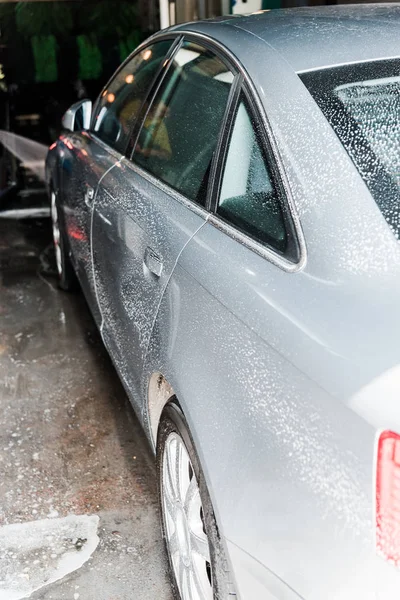 Selektiver Fokus des grauen Fahrzeugs mit weißem Schaum in der Waschanlage — Stockfoto