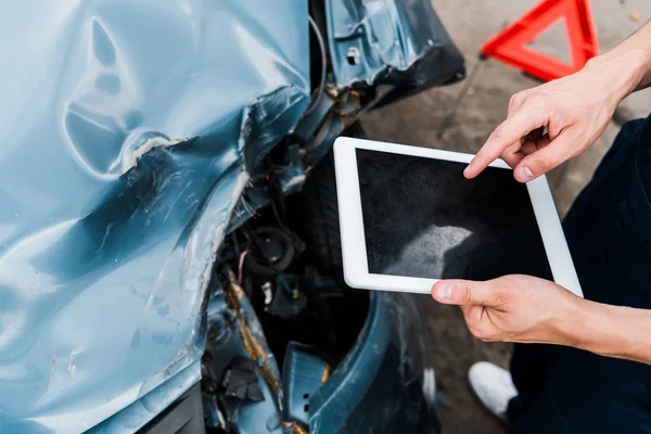 Ausgeschnittene Ansicht eines Mannes, der mit dem Finger auf ein digitales Tablet mit leerem Bildschirm in der Nähe eines abgestürzten Autos zeigt — Stockfoto