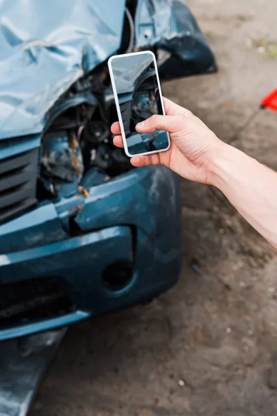 Vista recortada del hombre que sostiene el teléfono inteligente con la pantalla en blanco cerca del coche dañado — Stock Photo