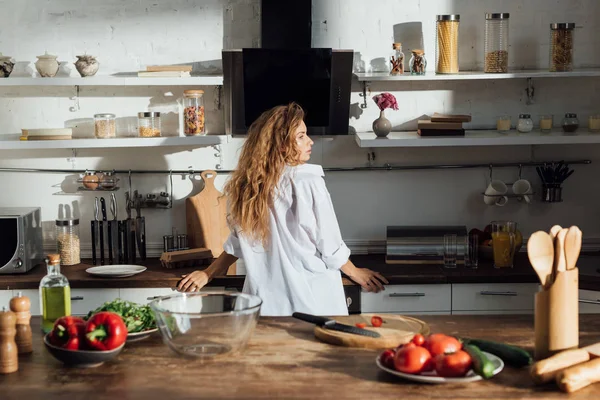 Jovem mulher de camisa branca em pé na cozinha e olhando para longe — Fotografia de Stock