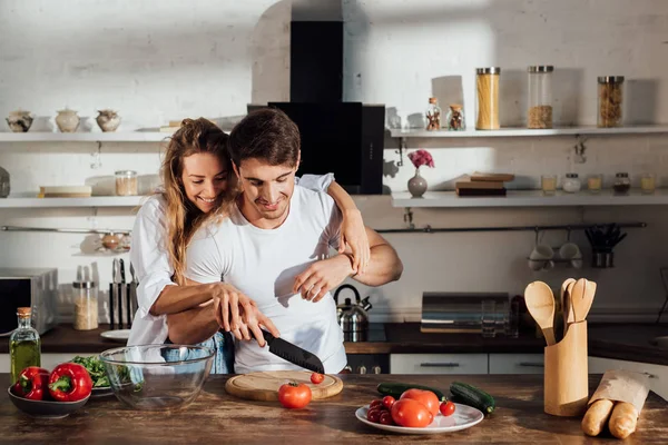 Feliz pareja sonriendo mientras cocinan juntos en la cocina - foto de stock