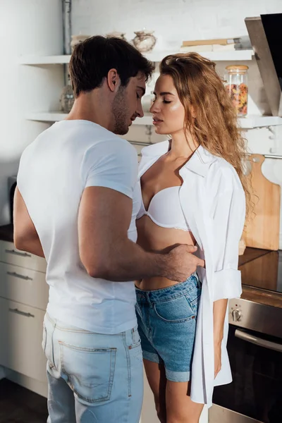 Muscoloso uomo in bianco t-shirt abbracciando fidanzata sexy in cucina — Foto stock