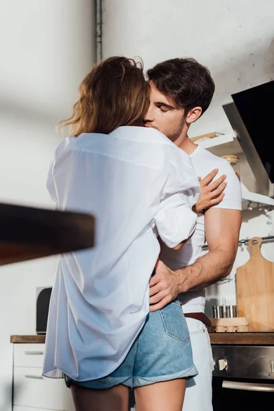 М'язистий чоловік обіймає сексуальну дівчину із закритими очима на кухні — стокове фото
