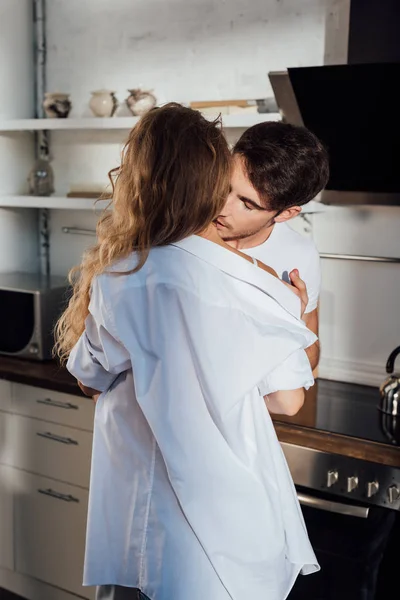 Man undressing girlfriend and kissing her in neck in kitchen — Stock Photo