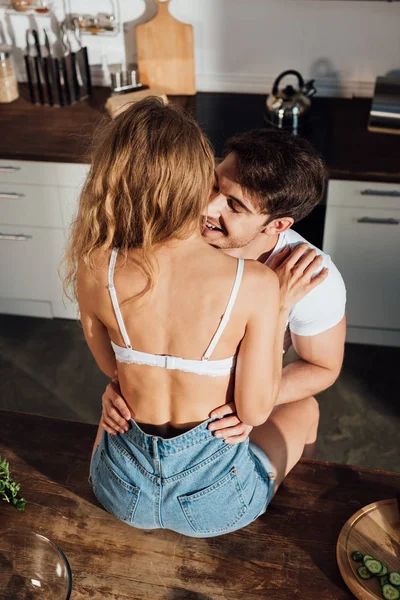 Overhead view of sexy girl sitting on table and embracing with boyfriend in kitchen — Stock Photo