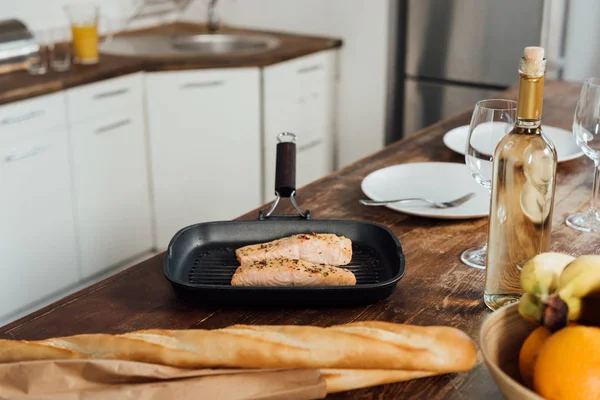 Fisch in der Pfanne, Obst, Baguette und Wein auf dem Tisch in der Küche — Stockfoto