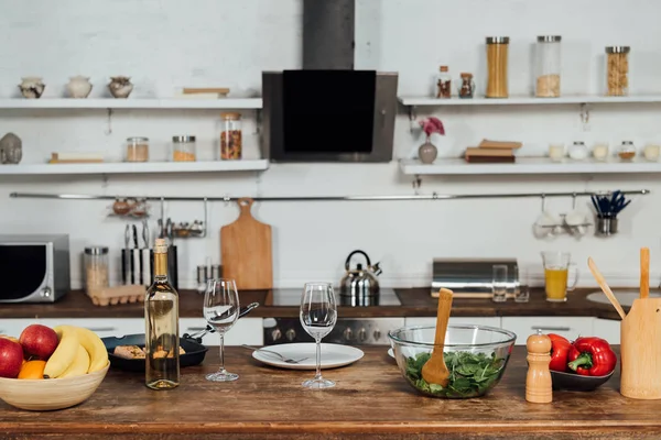 Свежие фрукты, перец, салат, рыба и вино на столе на кухне — стоковое фото