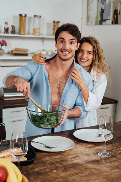 Happy couple embracing while cooking salad together in kitchen — Stock Photo