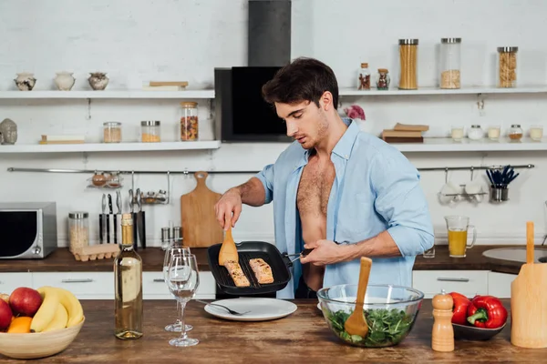 Sexy man holding frying pan with fish in kitchen — Stock Photo