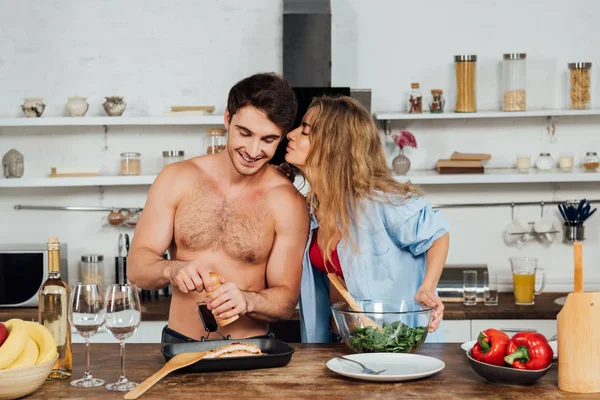 Sexy chica besando novio mientras él condimento plato en cocina - foto de stock