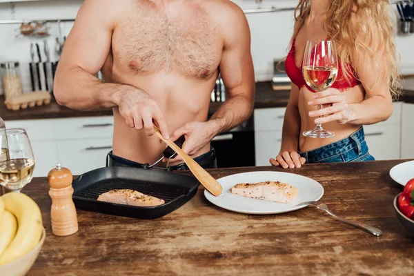 Corte vista de sexy menina segurando copo de vinho enquanto namorado cozinhar na cozinha — Fotografia de Stock