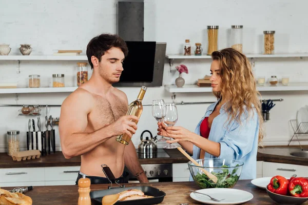 Casal sexy com vinho de pé perto da mesa com comida na cozinha — Fotografia de Stock