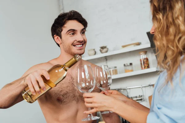 Улыбающийся мужчина без рубашки, стоящий рядом с сексуальной девушкой и наливающий вино в бокалы — стоковое фото