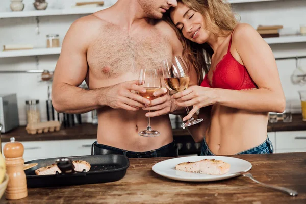 Cropped view of happy sexy couple holding wine glasses in kitchen — Stock Photo