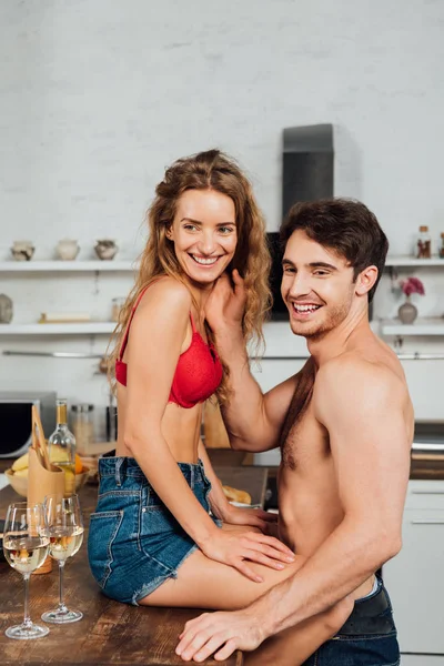 Sexy pareja desnuda sonriendo y mirando hacia otro lado en la cocina - foto de stock