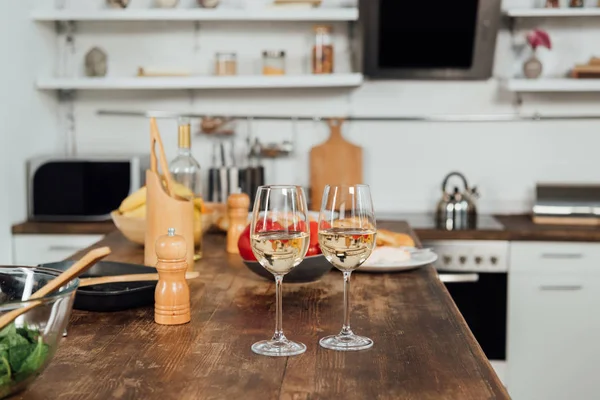 Wine glasses with wine, food and cooking utensils on table in kitchen — Stock Photo