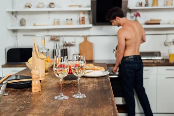 Enfoque selectivo del hombre sin camisa y la mesa con alimentos y copas de vino en primer plano - foto de stock