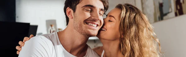 Panoramic shot of charming girl kissing boyfriend in cheek in kitchen — Stock Photo