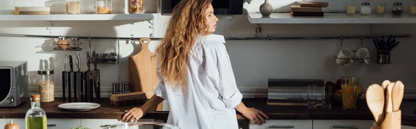 Panoramic shot of girl in white shirt standing in kitchen — Stock Photo