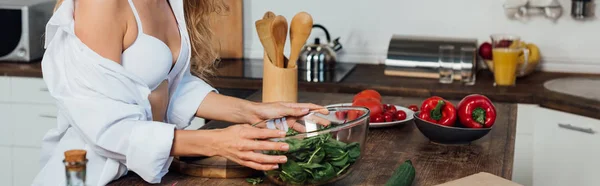 Panoramic shot of sexy girl in white bra cooking salad in kitchen — Stock Photo