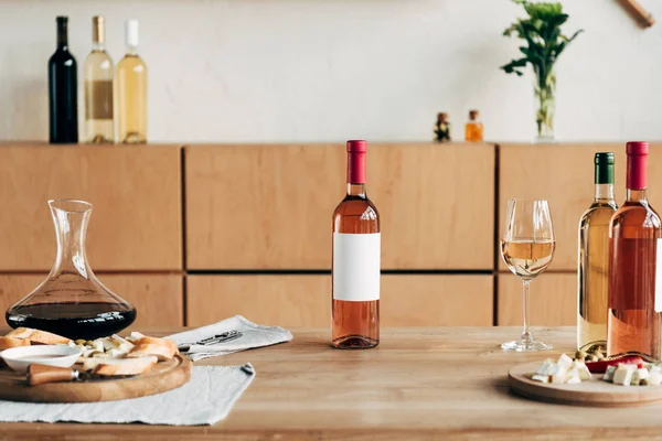 Botellas de vino, copa de vino y comida en mesa de madera - foto de stock